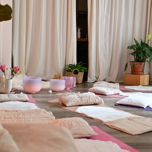 Pu&ograve; includere: Una stanza con tende bianche e pavimento in legno. Ci sono diverse coperte e cuscini sul pavimento, insieme a due ciotole cantanti di cristallo rosa e viola.
