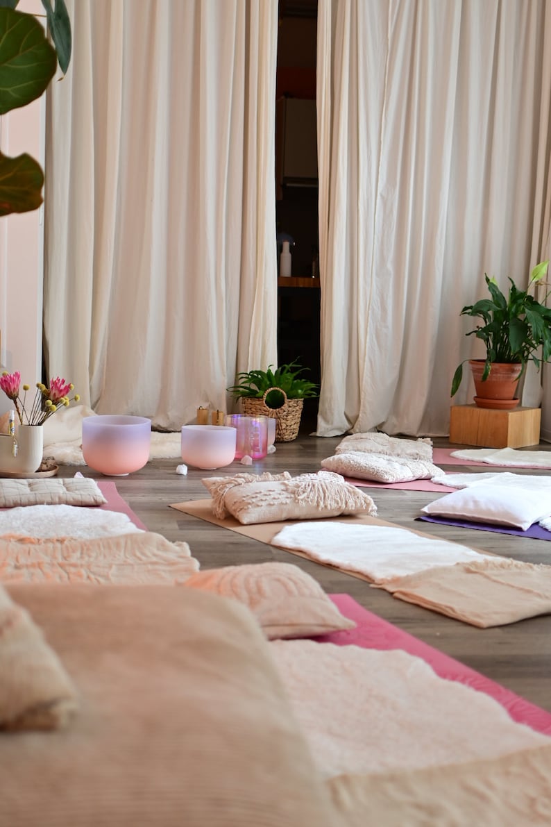 Pu&ograve; includere: Una stanza con tende bianche e pavimento in legno. Ci sono diverse coperte e cuscini sul pavimento, insieme a due ciotole cantanti di cristallo rosa e viola.