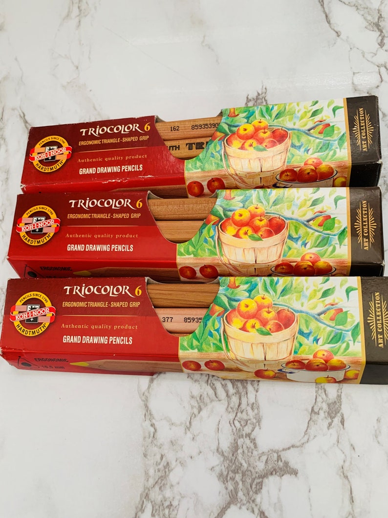 May include: Three boxes of Koh-I-Noor TrioColor 6 Grand Drawing Pencils. The boxes are red with the brand name and product information in white. Each box features a drawing of a basket of apples. The pencils have an ergonomic triangle-shaped grip.