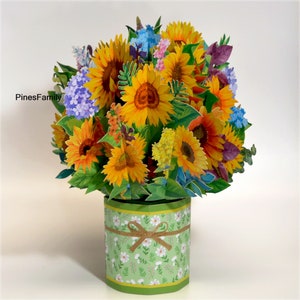 May include: A 3D pop-up card featuring a bouquet of yellow sunflowers, purple and blue flowers, and green leaves in a green and white patterned vase. The card is titled "PinesFamily".