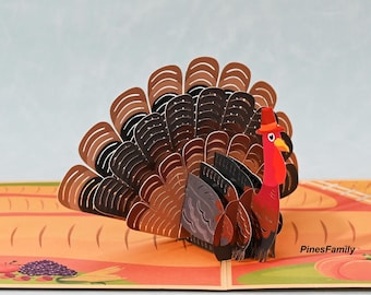 May include: A 3D pop-up card featuring a Thanksgiving turkey with a red, black, and brown patterned design. The turkey is standing on a brown and orange background with a field of wheat and a pumpkin.