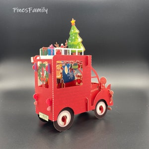 Pu&ograve; includere: Un biglietto pop-up rosso che raffigura un camion di consegna a tema natalizio con un albero di Natale decorato in cima. Il camion &egrave; pieno di decorazioni natalizie, un uomo di pan di zenzero e un piccolo orsacchiotto. Il camion ha una targa che recita "W2UHG".