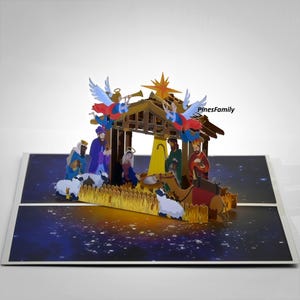 May include: A pop-up greeting card featuring a three-dimensional nativity scene with a wooden stable, a bright yellow star, two angels, and figures including Mary, Joseph, and the Three Wise Men. The base displays a dark blue starry night sky.