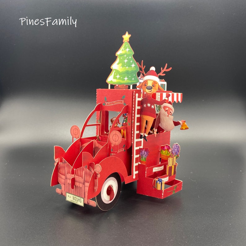 Pu&ograve; includere: Un camion rosso con un albero di Natale, una renna e Babbo Natale in cima. Il camion ha una targa che dice "WZUHG".