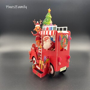 Pu&ograve; includere: Un camioncino rosso giocattolo con un albero di Natale, Babbo Natale e una renna in cima. Il camioncino ha una striscia bianca e una targa che dice "No. 1 WE WISH".
