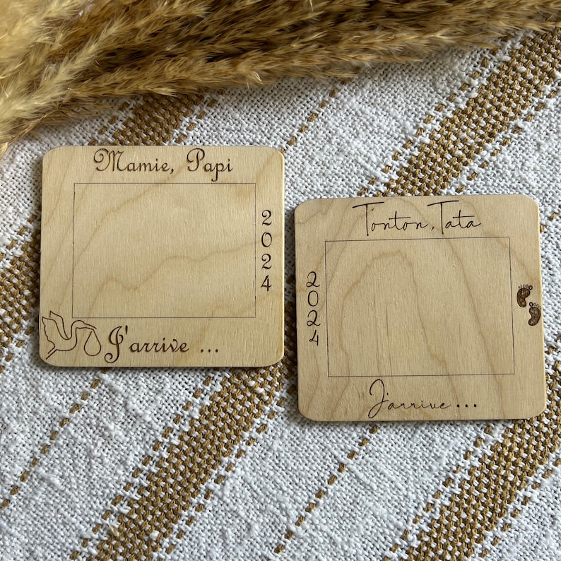 May include: Two wooden plaques with engraved text and a rectangular frame. One reads "Mamie, Papi 2024 J'arrive..." with a dove graphic. The other says "Tonton, Tata 2024 J'arrive..." with baby footprints.