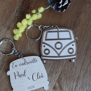 Peut inclure: Porte-clés en bois avec un design de van vintage. Le porte-clés est inscrit avec le texte "En vadrouille Paul & Cloé 2024".