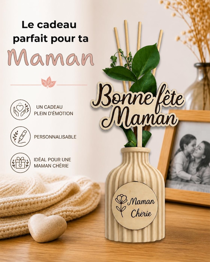 May include: A beige ribbed ceramic diffuser bottle with a wooden plaque reading Maman Ch&eacute;rie and a flower icon. A wooden topper reads Bonne f&ecirc;te Maman, accompanied by green leaves and wooden reeds. Text includes Le cadeau parfait pour ta Maman.