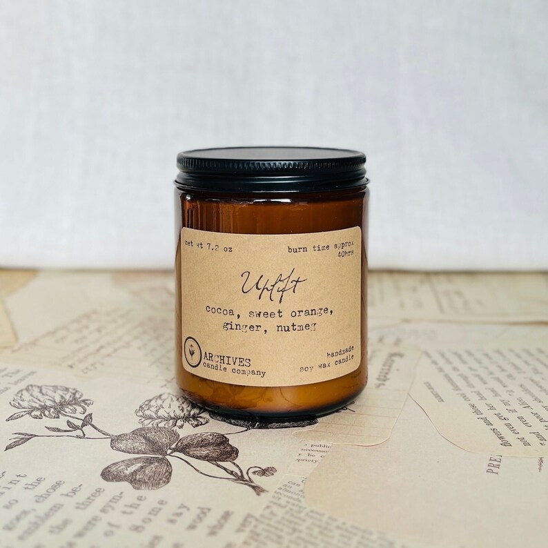 Photo of a glass jar candle with black lid and tan antique style label with script and typewriter fonts. Scented with sweet orange, chocolate, and ginger. Handmade small local business woman owned.