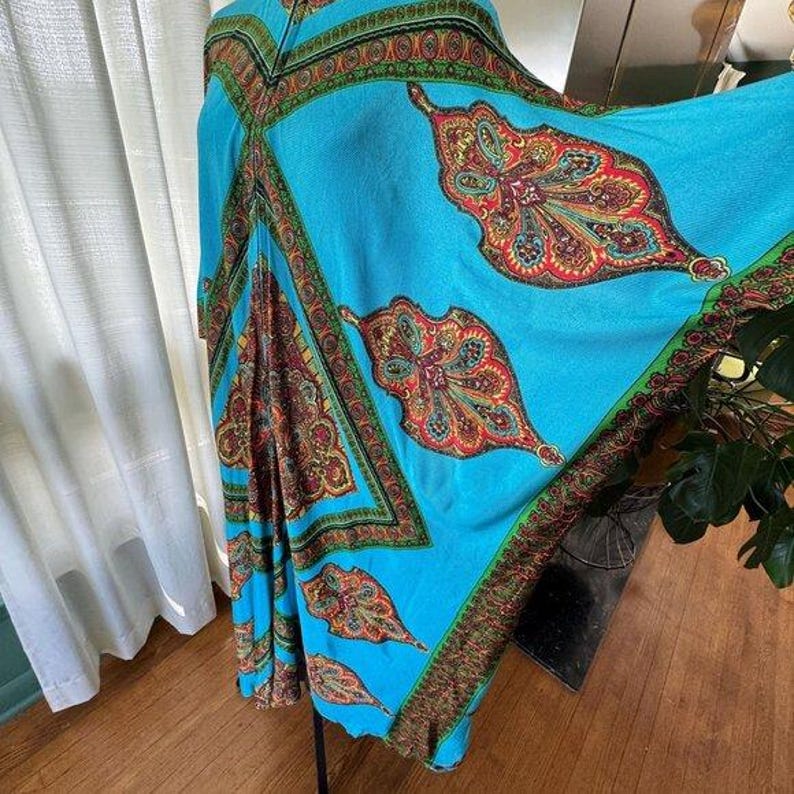 Puede incluir: Un caft&aacute;n de color turquesa brillante con un patr&oacute;n de cachemira repetitivo en tonos rojo, naranja y verde. La prenda tiene mangas anchas y fluidas, con un dise&ntilde;o de borde geom&eacute;trico que enmarca los paneles centrales de tela.