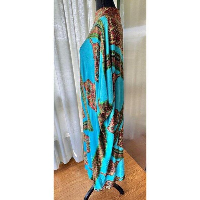 Puede incluir: Un vestido caft&aacute;n de color turquesa brillante con cuello alto y un patr&oacute;n de cachemira repetitivo en tonos rojo, dorado y marr&oacute;n oscuro. La prenda tiene mangas anchas y fluidas y una silueta recta y holgada que llega hasta la pantorrilla.