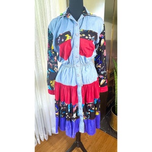 May include: A vintage denim dress with long sleeves, a button-down front, and a tiered skirt. The dress has red pockets and a red and black patterned skirt. The sleeves are black with a colorful pattern. The dress is displayed on a black mannequin.