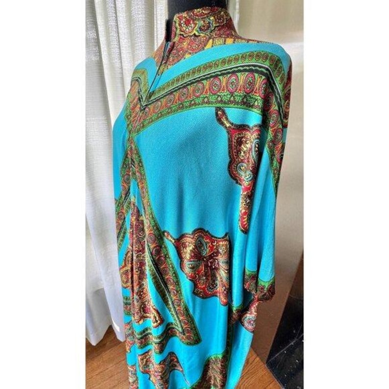 Puede incluir: Una t&uacute;nica de color turquesa brillante con cuello alto y un vibrante estampado de cachemira multicolor en tonos rojo, dorado y verde. La prenda tiene una silueta holgada y fluida con mangas anchas y un dise&ntilde;o de borde detallado en el cuello.