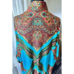 Puede incluir: Una blusa de cuello alto con un vibrante estampado de cachemira en tonos turquesa, rojo, dorado y verde. La prenda presenta un dise&ntilde;o sim&eacute;trico e intrincado con una prominente banda turquesa en forma de V sobre el pecho y los hombros.
