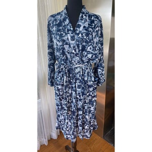 May include: A long-sleeved robe with a geometric pattern in shades of blue, white, and gray. The robe has a V-neck, a matching belt, and pockets. The garment is displayed on a mannequin.
