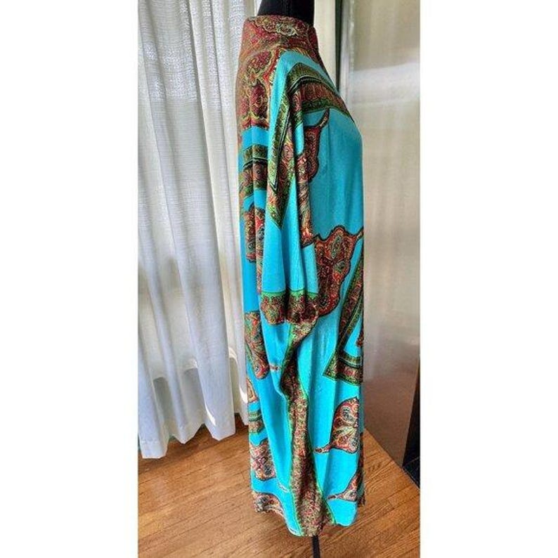 Puede incluir: Un vestido tipo t&uacute;nica de manga larga en un vibrante color base azul turquesa, con un llamativo estampado de cachemira multicolor en tonos rojo, dorado y verde. La prenda tiene un cuello alto y una silueta holgada y fluida.