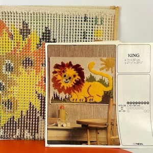 May include: Vintage needlepoint kit featuring a lion design. The kit includes a partially completed needlepoint canvas and a pattern with the word "KING" and measurements of approximately 27" x 19". The lion has a yellow body and a brown mane.