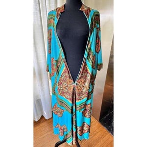 Puede incluir: Un caft&aacute;n largo abierto por delante con una base de color turquesa vibrante y un patr&oacute;n ornamental repetitivo en tonos naranja, dorado y marr&oacute;n oscuro. La prenda tiene mangas cortas y anchas y un escote en V profundo y sim&eacute;trico.
