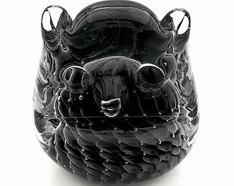 May include: A black glass sculpture of a stylized creature with large eyes and ear-like protrusions. The glass has a marbled appearance with small air bubbles throughout, giving it a unique texture. The sculpture is set against a white background.