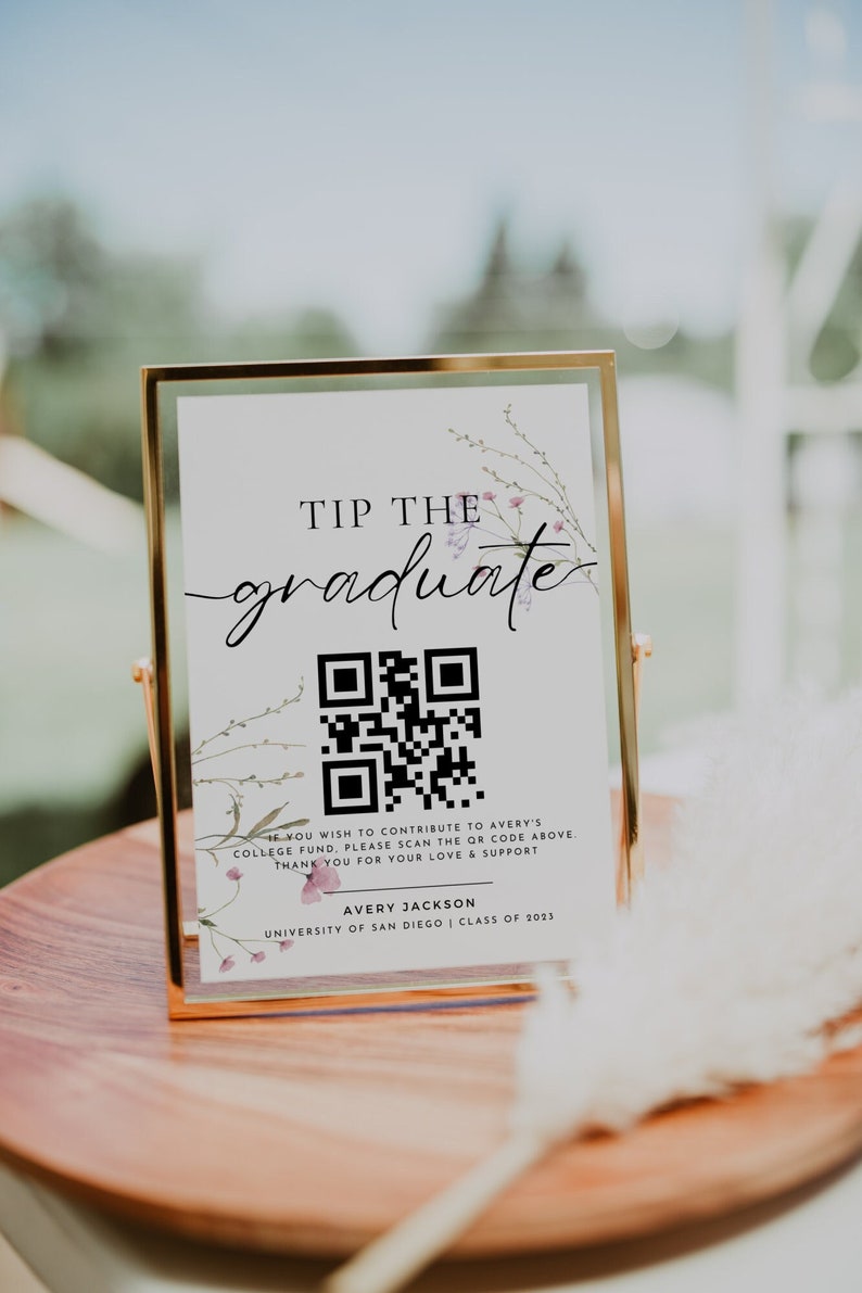 May include: A white sign with a gold frame and floral accents reads "Tip the graduate". A QR code is displayed below the text. The sign also includes the text "If you wish to contribute to Avery's college fund, please scan the QR code above. Thank you for your love & support. Avery Jackson, University of San Diego, Class of 2023."