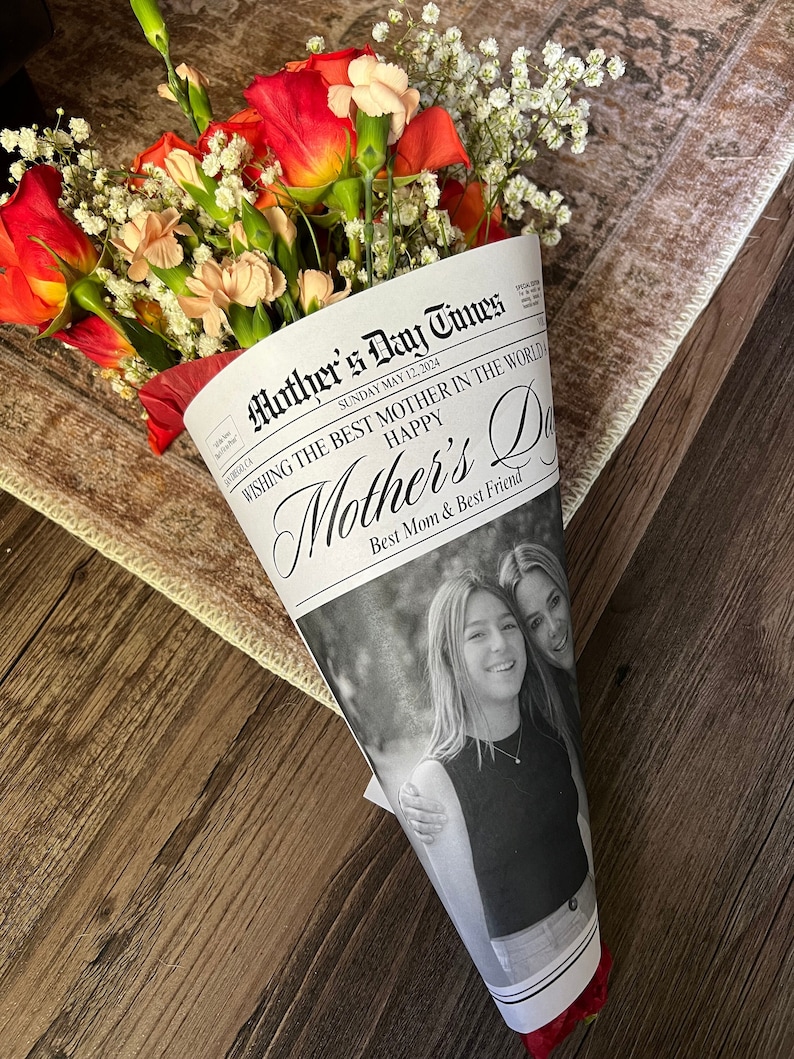 Puede incluir: Un ramo de flores rosas y naranjas envuelto en un cono de peri&oacute;dico con el titular "Mother's Day Times" y el texto "Wishing the best mother in the world Happy Mother's Day Best Mom & Best Friend".