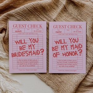 May include: Two pink cards with a grid pattern and red text. The text on the cards reads "Guest Check" and "Will you be my bridesmaid?" and "Will you be my maid of honor?"