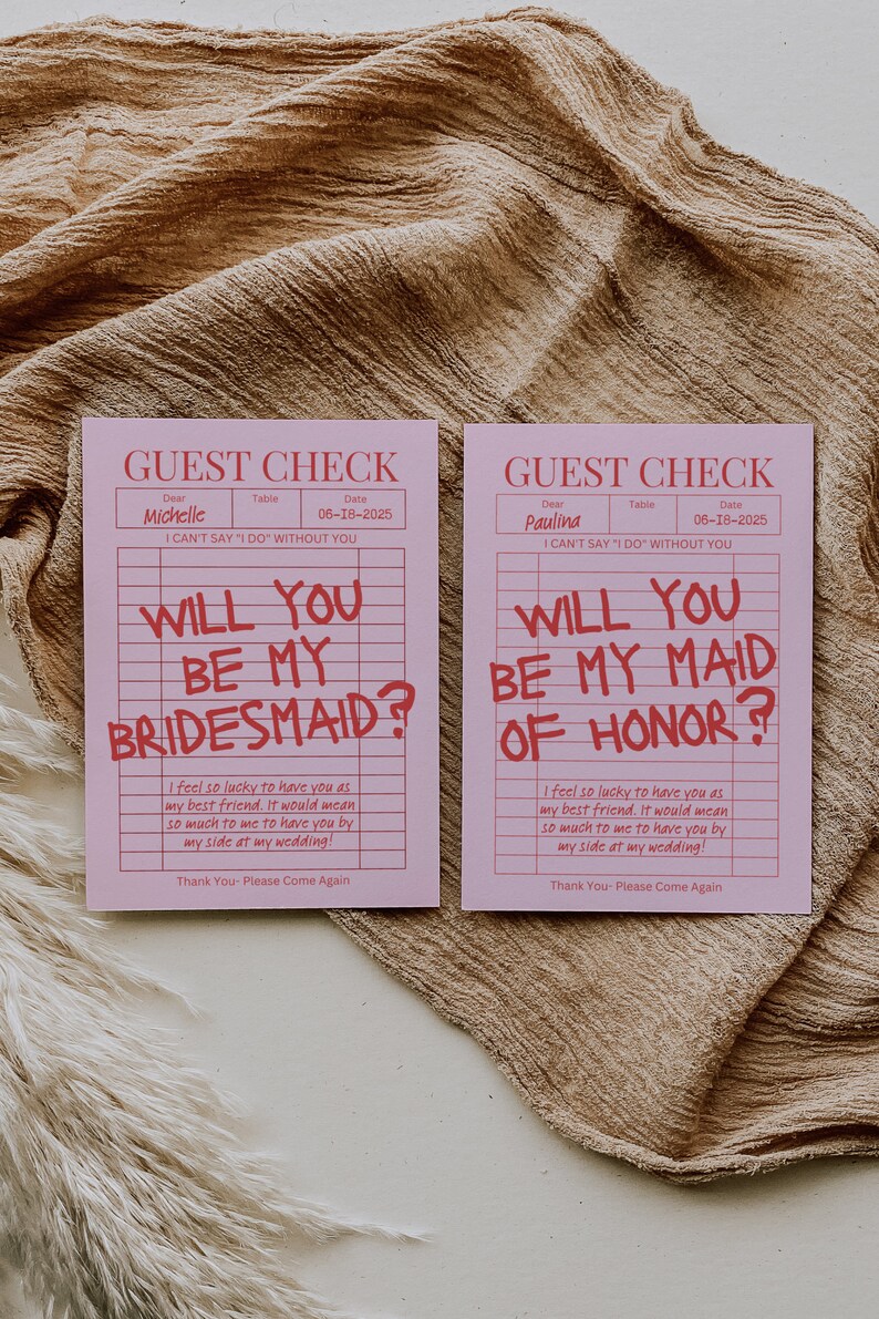 May include: Two pink cards with a grid pattern and red text. The text on the cards reads "Guest Check" and "Will you be my bridesmaid?" and "Will you be my maid of honor?"