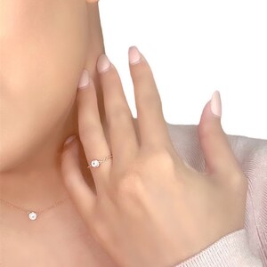 May include: A delicate gold necklace and ring set with a small, clear gemstone in the center of each piece.