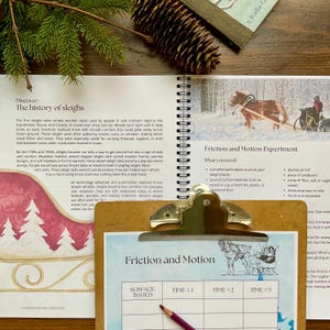 May include: A clipboard with a printed experiment sheet titled "Friction and Motion" sits on a wooden surface. The sheet has a table for recording data. A pencil rests on the table. A book with text about the history of sleighs is also visible.