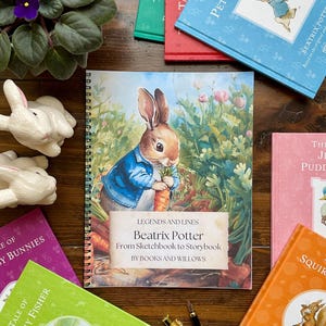 May include: A collection of Beatrix Potter books and related items. The central image is a spiral-bound book featuring Peter Rabbit. Surrounding it are several colorful books, ceramic bunnies, and pens. The book cover reads "Beatrix Potter From Sketchbook to Storybook".