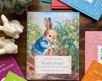 May include: A collection of Beatrix Potter books and related items. The central image is a spiral-bound book featuring Peter Rabbit. Surrounding it are several colorful books, ceramic bunnies, and pens. The book cover reads "Beatrix Potter From Sketchbook to Storybook".