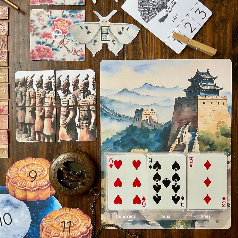 May include: A watercolor painting of the Great Wall of China with a traditional Chinese building in the background.  Three cards are displayed below the painting, showing the numbers 6, 9, and 3, representing hundreds, tens, and ones.  The cards are labeled with the words "hundreds", "tens", and "ones".