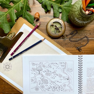 Puede incluir: Vista cenital de una br&uacute;jula antigua, l&aacute;pices y un mapa titulado "Heartwood Hotel Map". La escena incluye bellotas, hojas de roble y una peque&ntilde;a maceta de cer&aacute;mica verde llena de l&aacute;pices de colores, creando una est&eacute;tica r&uacute;stica y aventurera.