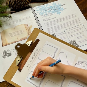 May include: A clipboard with a worksheet titled "Text Connections" is being used. A blue pencil is held by a hand, drawing on the worksheet. An open book with text and illustrations is visible in the background, along with a spiral-bound book.