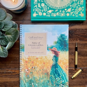Puede incluir: Un cuaderno de espiral con el título "Anne of Green Gables" y una ilustración en acuarela de una mujer en un campo. También se ve un libro de tapa dura con el mismo título y una pluma dorada. Una vela encendida y una planta en maceta están en el fondo.