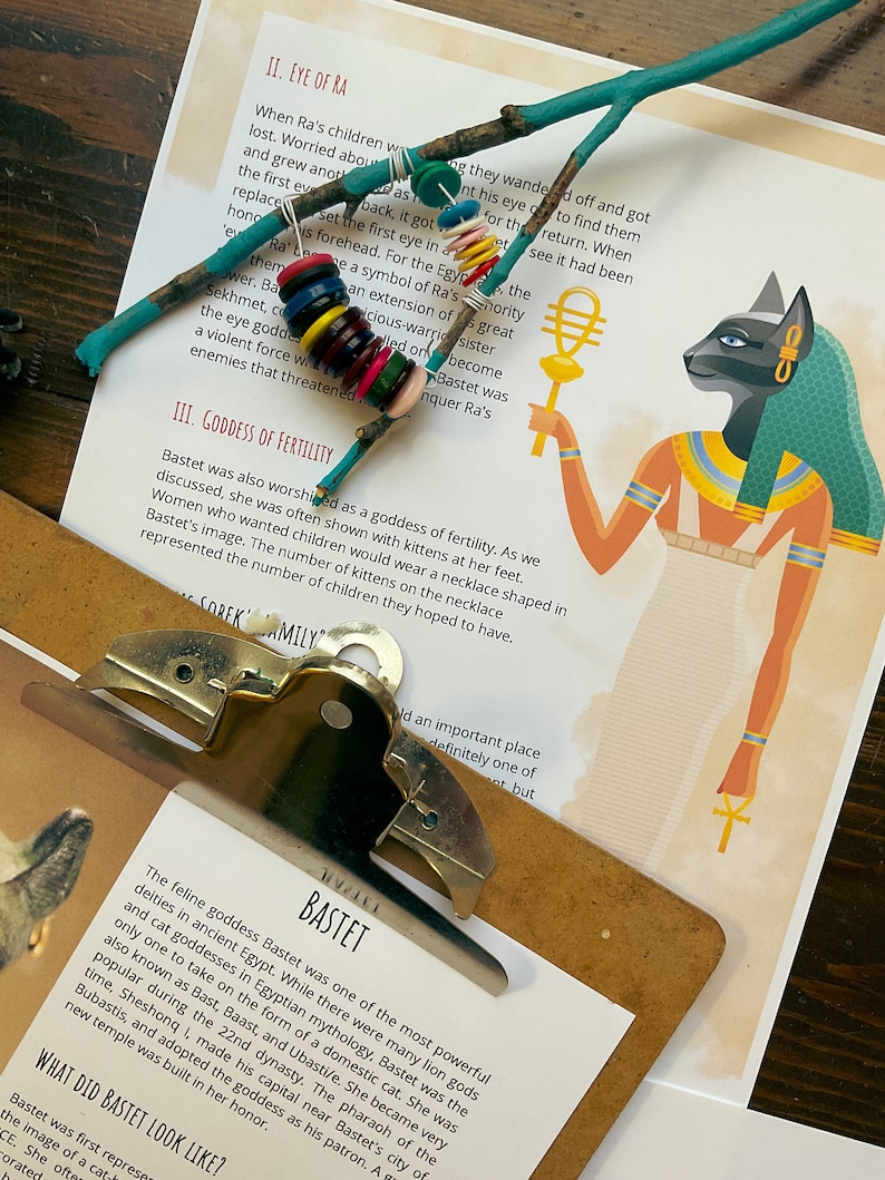 May include: Close-up of a page from a book about the Egyptian goddess Bastet. The page features a colorful illustration of Bastet, a cat-headed goddess, holding a staff. The text on the page discusses Bastet's role as a goddess of fertility and her association with cats.