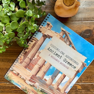 Puede incluir: Cuaderno de espiral con una portada que presenta una ilustración de columnas griegas antiguas bajo un cielo azul. El cuaderno está etiquetado como "History-Ink Adventures Ancient Greece A Research Notebook."