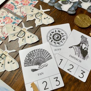 May include: A set of four cards with Chinese-inspired illustrations and numbers 1, 2, and 3 printed on each card. The illustrations include a fan, a zodiac wheel, an emperor, and a moth.