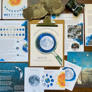 May include: A set of educational cards about the moon, featuring illustrations of the moon in different phases, a moon map, and a magnifying glass with a blue and white moon inside. The cards are titled "Looking Glass Nature Study: Moon" and "Moon Phases".