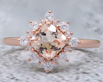 Könnte beinhalten: Ein Verlobungsring aus Roségold mit einem kissenförmigen Pfirsich-Morganit-Edelstein, umgeben von einem Heiligenschein aus kleineren runden Diamanten.