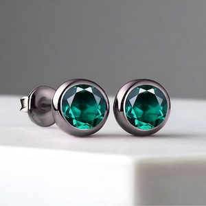 May include: A pair of black stud earrings with emerald green gemstones.