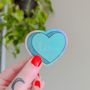 May include: A teal blue heart-shaped sticker with a holographic finish. The sticker has the word "Love" written inside the heart.