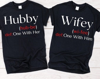 May include: Two black t-shirts with white text. The left shirt says "Hubby (hub-be) def: One With Her". The right shirt says "Wifey (wi-fee) def:One With Him".