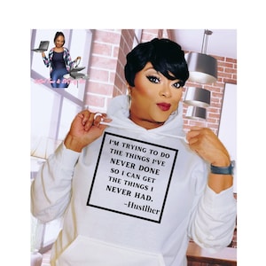 Może przedstawiać: Biała bluza z kapturem z czarnym kwadratem z przodu, na którym widnieje napis "I'm trying to do the things I've never done so I can get the things I never had. -Hustlher"