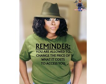 May include: A woman wearing a green t-shirt with the text "REMINDER: YOU ARE ALLOWED TO CHANGE THE PRICE OF WHAT IT COSTS TO ACCESS YOU". She is also wearing a green hat and has dark hair.