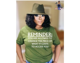 May include: A woman wearing a green t-shirt with the text "REMINDER: YOU ARE ALLOWED TO CHANGE THE PRICE OF WHAT IT COSTS TO ACCESS YOU" printed on it. She is wearing a green fedora hat and has dark curly hair.