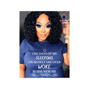 Op de afbeelding: Een vrouw met donker krullend haar en blauwe oogschaduw draagt een donkerblauw T-shirt met de tekst "The days of me sleeping on myself are over. Woke is the new me."