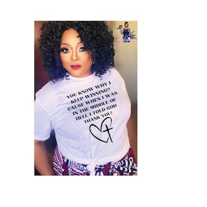 Puede incluir: Camiseta blanca con un gráfico negro que dice "¿Sabes por qué sigo ganando? Porque cuando estaba en medio del infierno le dije a Dios gracias!" y un corazón negro con una cruz dentro.