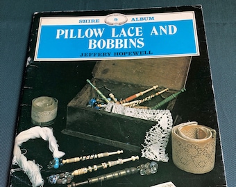 May include: A book titled "Pillow Lace and Bobbins" by Jeffery Hopewell. The book cover features a wooden box filled with bobbins and lace, along with a piece of lace and a spool of thread.