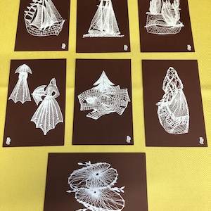 May include: Seven brown cards featuring white line drawings of sailboats, abstract forms, and figures. The cards are displayed on a yellow surface, offering a striking contrast. The drawings are detailed and intricate.